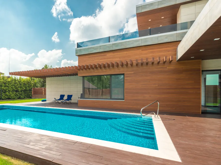 Piscina y terraza de madera junto a vivienda con revestimiento de madera